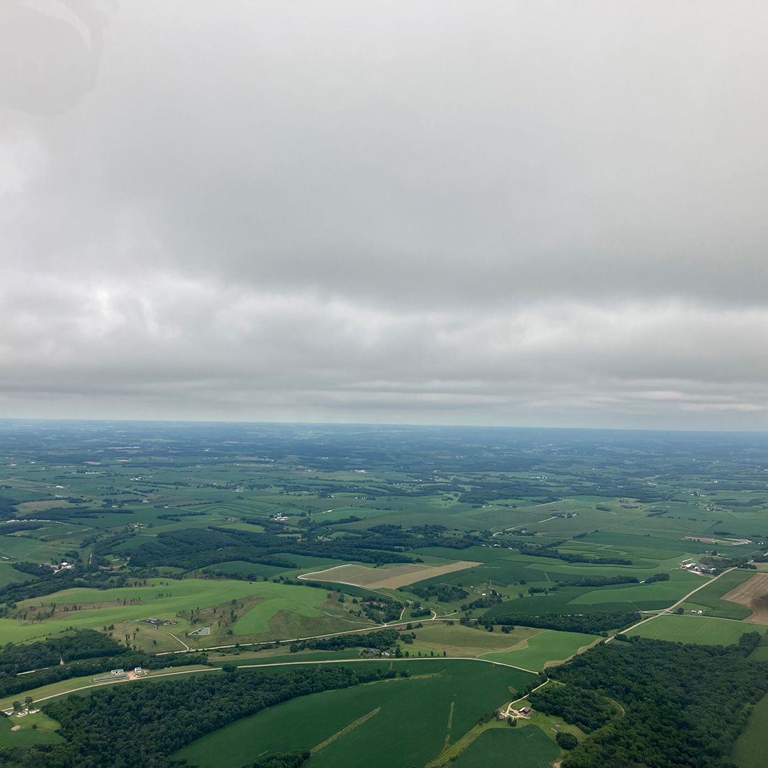 view of green farmland and gray skies from cessna
