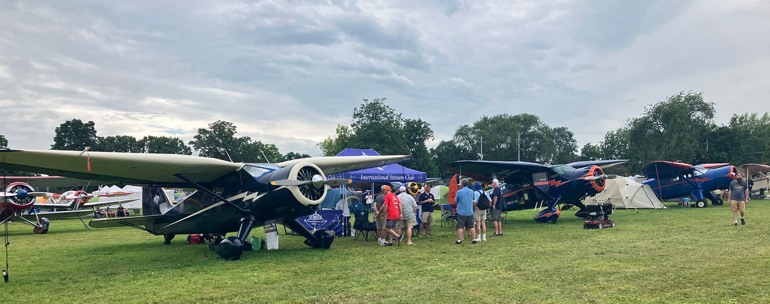 three blue stinson reliants on the grass with crowds gathered around