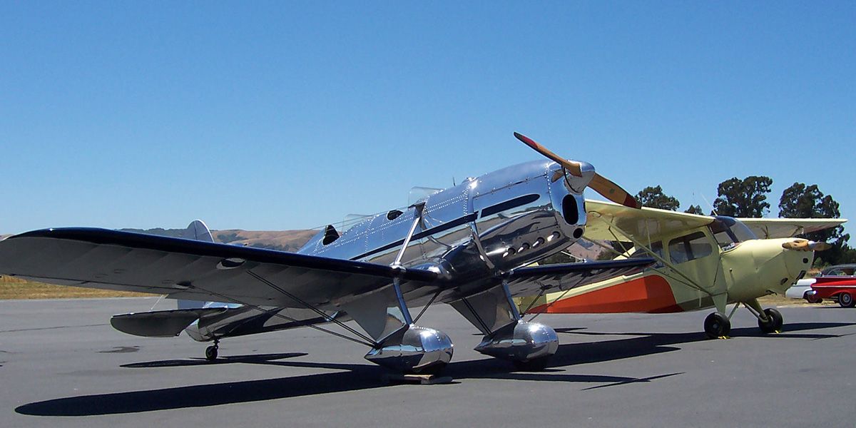 silver open cockpit stainless steel vintage plane in front of yellow and orange vintage plane